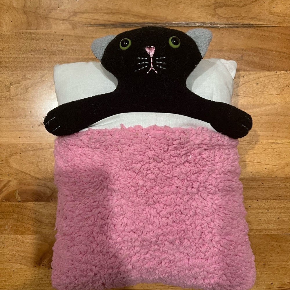 Black Cat Plush Tucked in Pink and Brown Bed Blanket